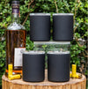 Set of four dark insulated whiskey lowball tumblers on a wood outdoor stump