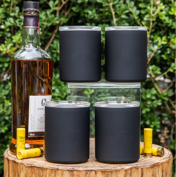 Set of four dark insulated whiskey lowball tumblers on a wood outdoor stump