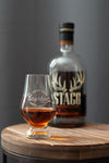 Bourbon tasting glass with amber drink and engraved logo, beside bottle on wood