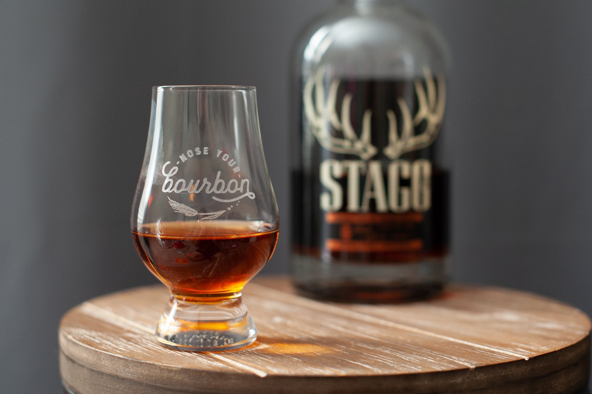 Stemmed bourbon tasting glass, tulip shape with amber liquid on wooden board