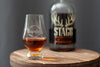 Stemmed bourbon tasting glass, tulip shape with amber liquid on wooden board