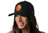 Black trucker cap with orange crossed-clubs leather patch, worn by woman