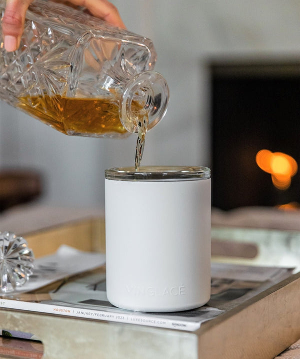 White glass-lined lowball whiskey tumbler with whiskey being poured into the cup