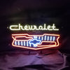 Neon car logo sign with Chevrolet script and grille outline lights in blue, orange, white
