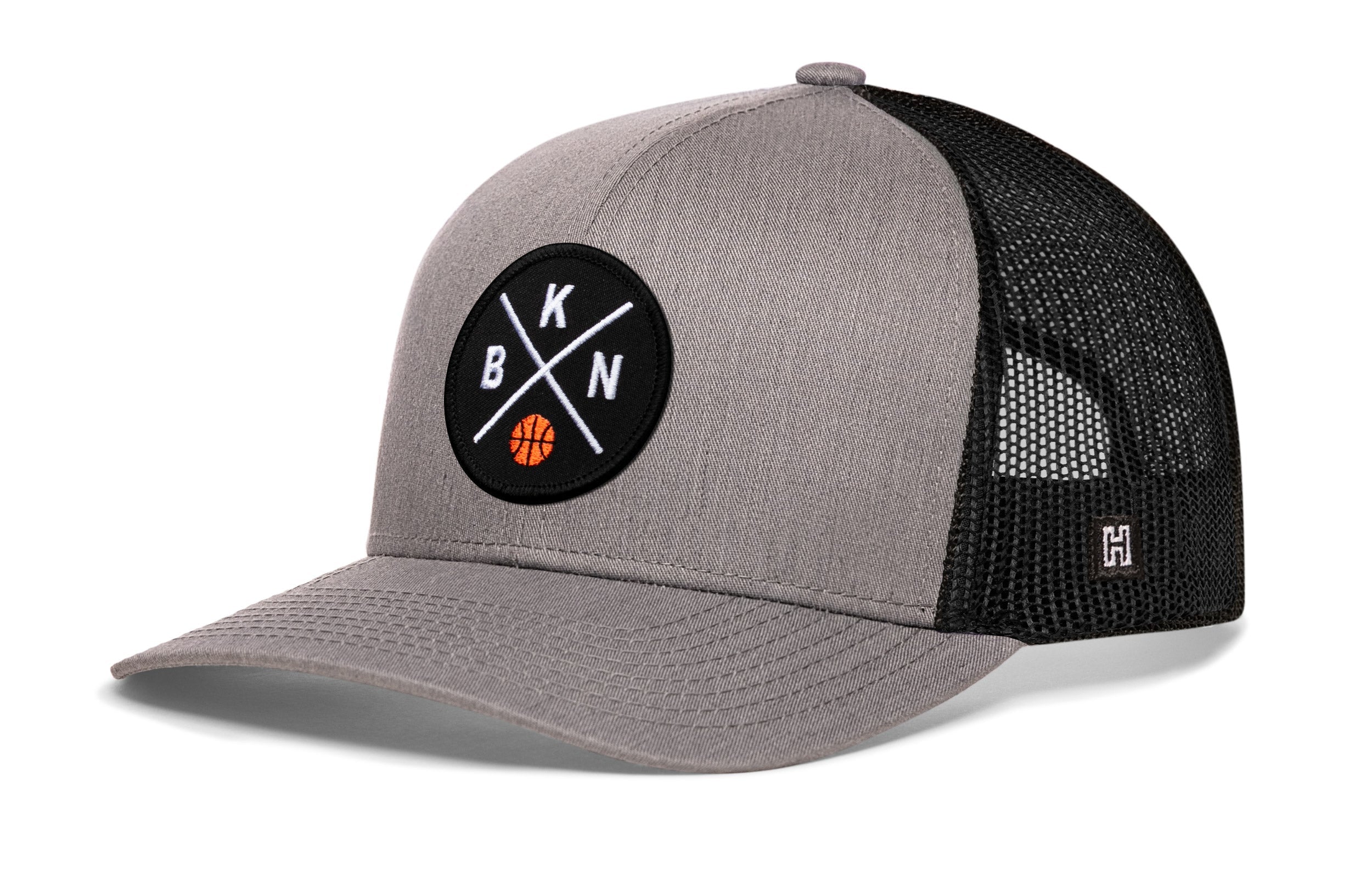 Gray trucker cap with front circular logo patch, black mesh side panels, curved brim