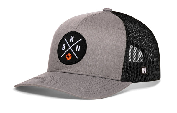 Gray trucker cap with front circular logo patch, black mesh side panels, curved brim