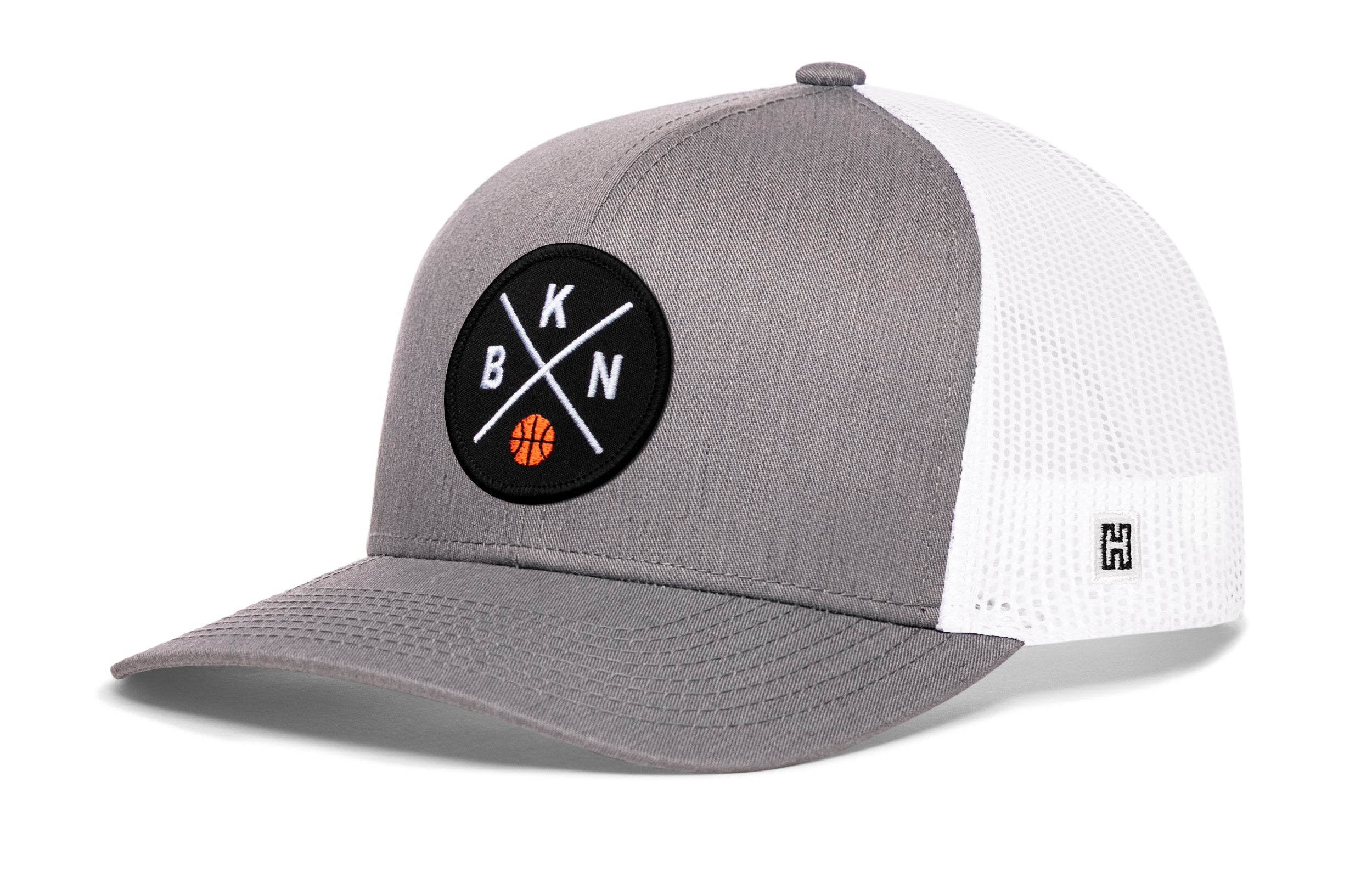 Gray trucker cap with circular front logo patch and white mesh side panels, curved brim