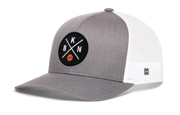 Gray trucker cap with circular front logo patch and white mesh side panels, curved brim