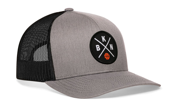 Gray front trucker cap with circular logo patch, black mesh side panels, curved brim