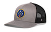 Gray-and-black trucker snapback hat with front circular logo patch and mesh back panel.