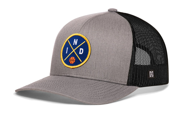 Gray-and-black trucker snapback hat with front circular logo patch and mesh back panel.
