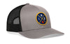Gray-and-black trucker snapback hat with front-right circular logo patch and mesh back panel.