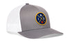 Gray-and-white trucker snapback hat with front-right circular logo patch and mesh back panel.