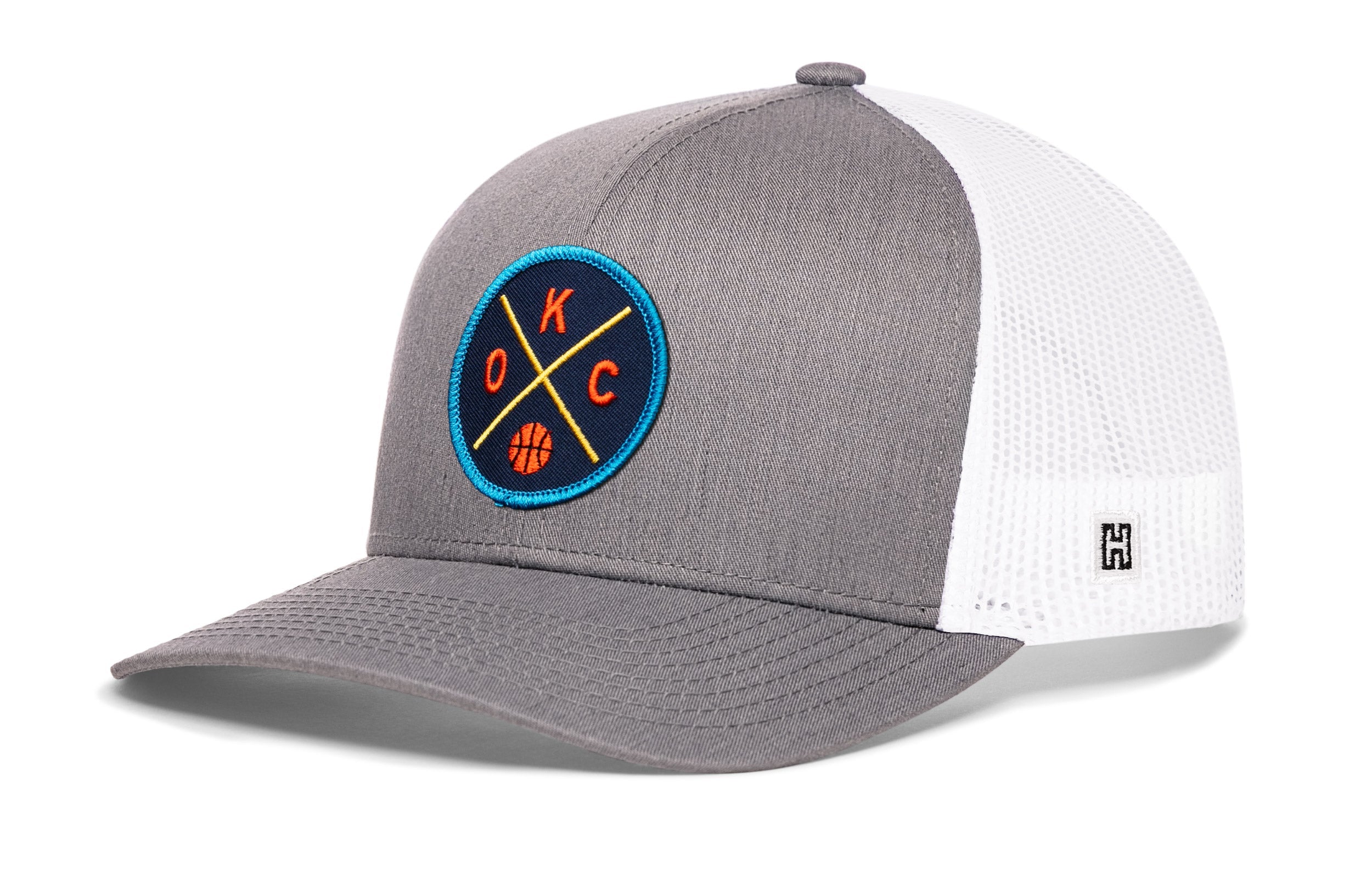 Gray and white trucker hat with mesh sides, curved brim, and circular team logo patch.