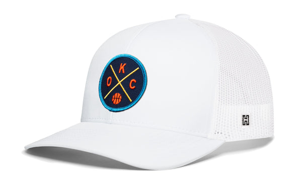 White trucker hat with mesh sides, curved brim, and circular team logo patch.