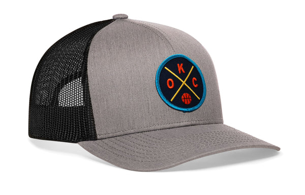 Gray and black trucker hat with mesh sides and circular team logo patch on the front.