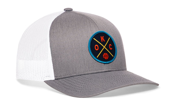 Gray and white trucker hat with mesh sides and circular team logo patch on the front.