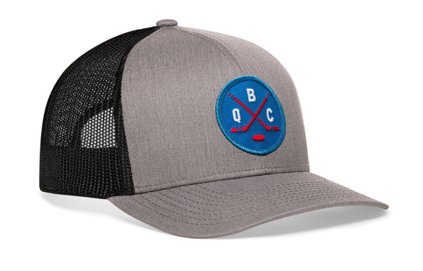 Gray hockey trucker cap with blue front logo patch, black mesh side panels, curved brim