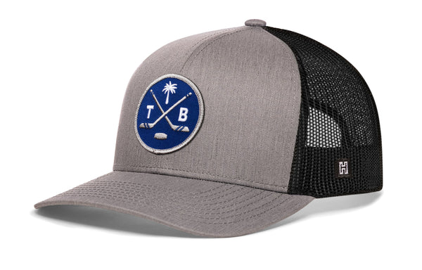 Gray trucker hat with blue circular logo patch, black mesh sides, and small H tag