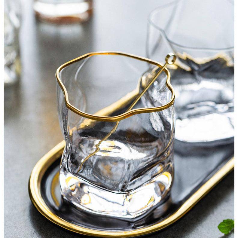 Gold-rim crystal whisky glass on a gold tray with a small amber pool