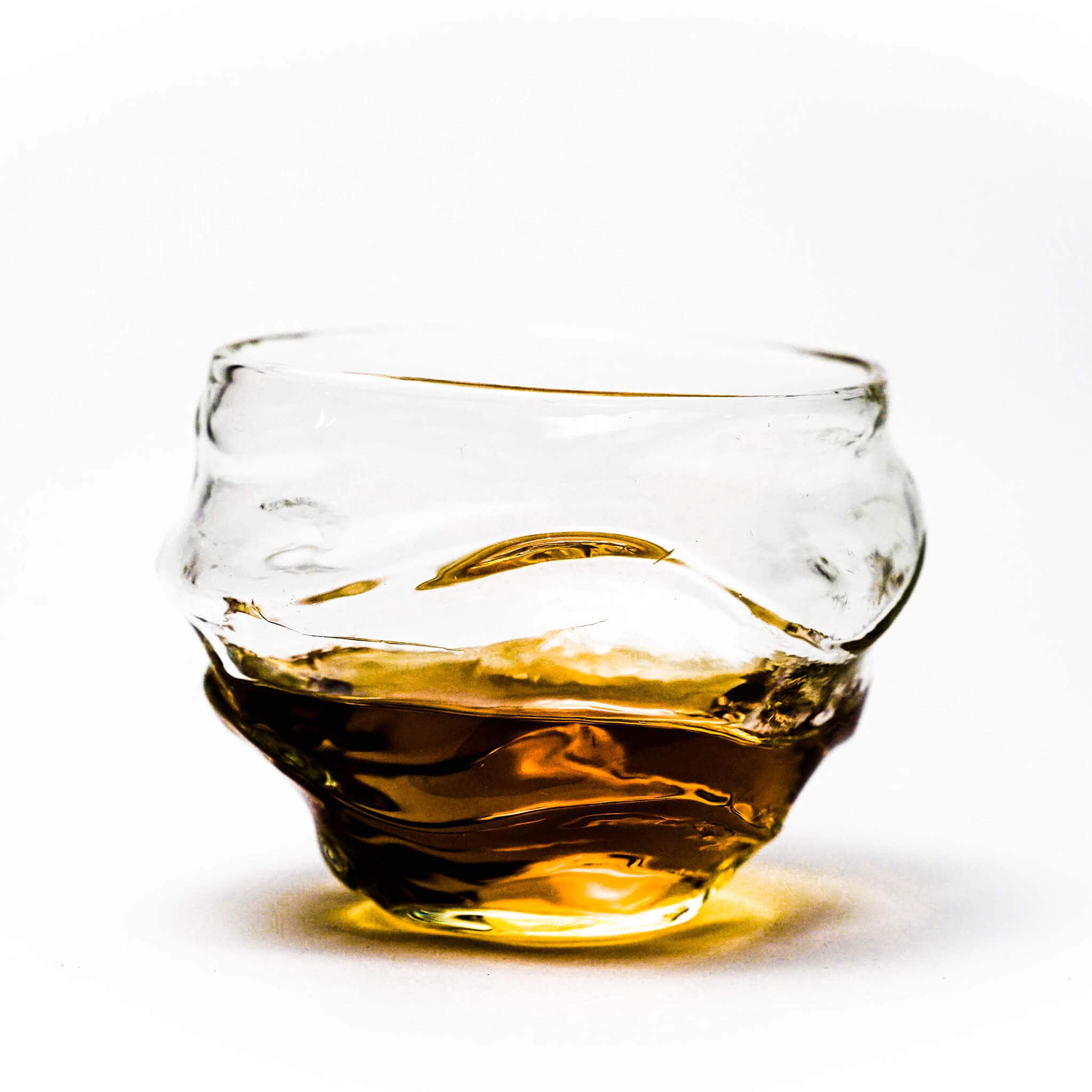 Crystal whisky glass with amber base liquid and clear wavy top rim.